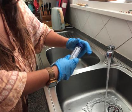 Person in blue gloves holding a water sample tube.